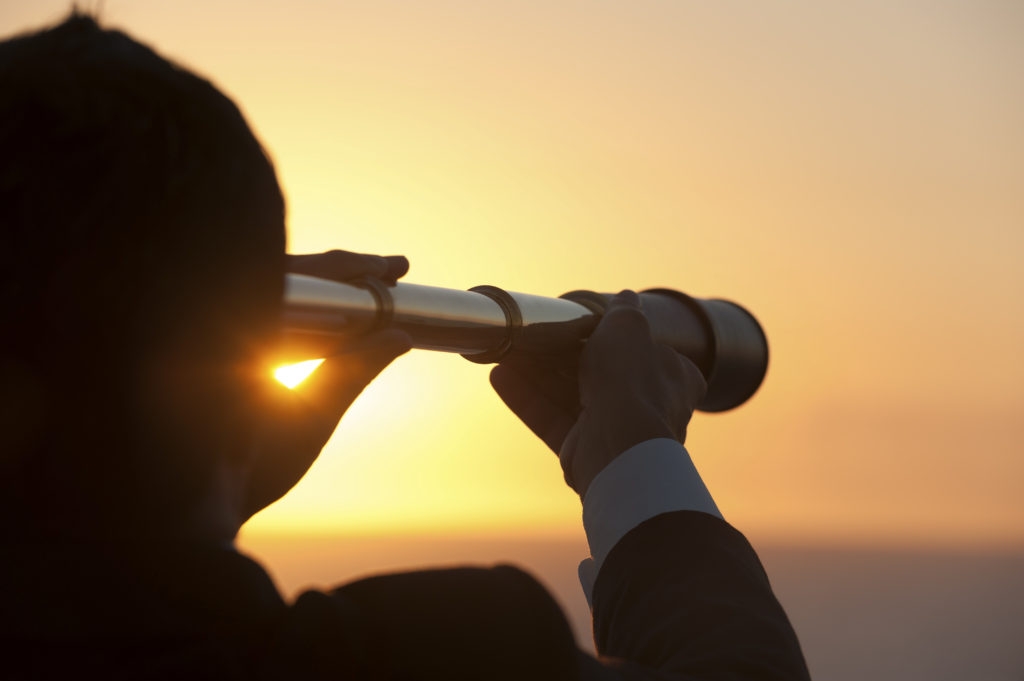 Businessman looking to the future with telescope at sunrise